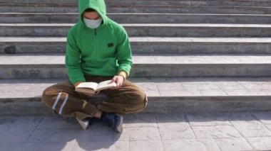 Genç adam salgın sırasında sokakta kitap okuyor.