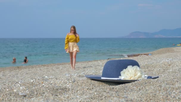 Descansando senhora em trajes de praia segurando curso para palha chapéu elegante na praia de seixos — Vídeo de Stock