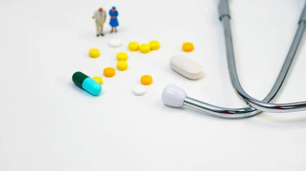 Minyatür bir kadın, minyatür bir adam ilaçları ve beyaz arka planda Doktor 'un kulaklıkları. Sağlık hizmeti kavramı. Ve yaşlılıkta tıbbi bakım..