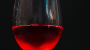 Şarap kadehi ve kırmızı su kabarcıkları siyah arkaplanda.