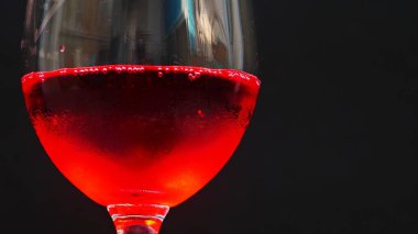 Şarap kadehi ve kırmızı su kabarcıkları siyah arkaplanda.