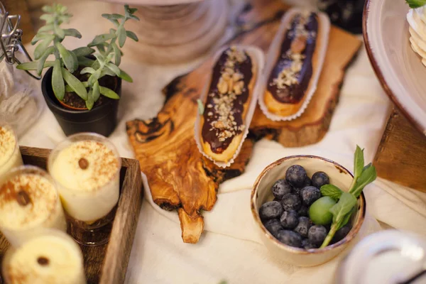 Godis-bar med eclairs, blåbär och grönska på träbricka. S — Stockfoto
