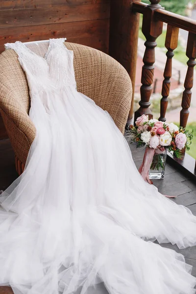 Robe de mariée blanche couchée sur fauteuil sur balcon en bois avec bea — Photo