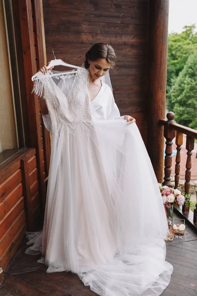 Feliz novia tratando de vestirse de blanco en el balcón de madera en la boda m —  Fotos de Stock