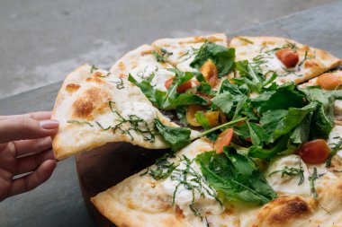 Kadın eli, üzerinde domates, peynir ve fesleğen olan taze İtalyan pizzasından bir parça alır. Uzayı kopyala Sevgiyle ev yapımı. Hızlı teslimat. Yemek tarifi ve menü. Üst görünüm.