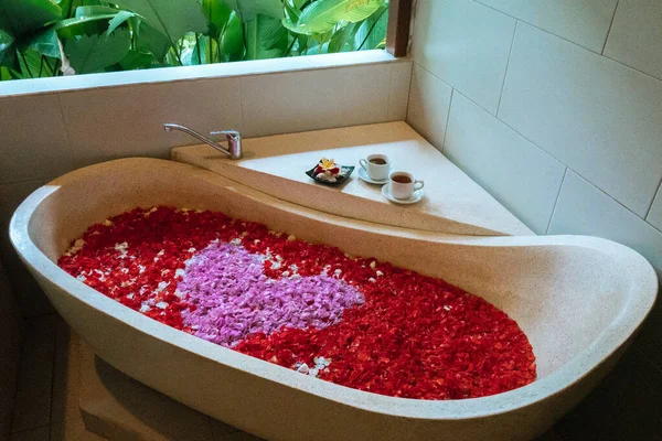Bañera de piedra con pétalos de flores en forma de corazón cerca de la ventana con vista a la selva. Relajación de spa orgánico en baño de lujo Bali . —  Fotos de Stock