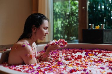 Kadın ellerinde çiçek kokusundan hoşlanıyor. Açık havada banyo yapıyor. Tropik çiçekler, organik cilt bakımı, lüks bir spa oteli, yaşam tarzı fotoğrafı.