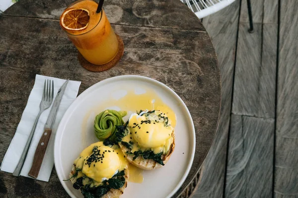 Ovanifrån av hälsosam frukost med bröd toast och pocherade ägg med spenat, avokado på träbord och apelsinsmoothie på bakgrunden. — Stockfoto