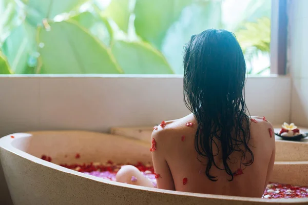 Widok z tyłu kobiety relaks w okrągłej kąpieli na zewnątrz z tropikalnych kwiatów, ekologicznej pielęgnacji skóry, luksusowy hotel uzdrowiskowy, styl życia Zdjęcia — Zdjęcie stockowe