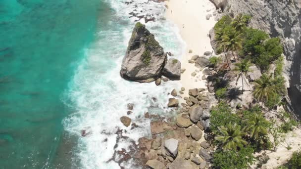 熱帯のビーチ、海の岩、ターコイズブルーの海とヤシの木の空中ドローンの写真。アトゥビーチ、ヌサペニダ島、バリ、インドネシア。熱帯の背景と旅行の概念 — ストック動画