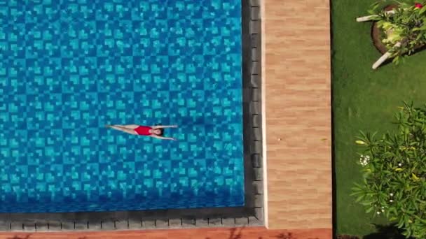 Top view of slim woman in red bikini swimming on back and relaxing in blue swimming pool and get out. Vacation concept. Aerial veiw. Drone — Stock Video