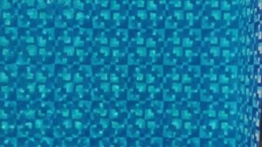 Aerial- mavi yüzme havuzu. Güneş ışığı altında üst manzaralı. Su yüzeyinde dalgalanma ve yaz tatilinde mavi mozaik fayans..