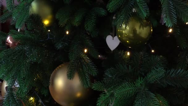 Nahaufnahme von Weihnachtsbaumdetails mit Ornamenten aus Christbaumkugeln, Schneeflocken, goldenen Kugeln, herzförmigem Derokor und Lichtern aus Girlanden — Stockvideo