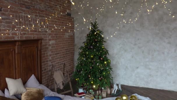 Stylowe wnętrze poddasza Bożego Narodzenia, przytulna sypialnia z drewnianym łóżkiem i wiele świateł z urządzoną choinką i girlandą. — Wideo stockowe