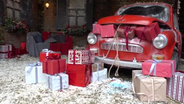 Nowy Rok urządzone na zewnątrz z bagażnika pełnego prezentów świątecznych retro czerwony samochód ze śniegiem i świąteczne światła i girlandy poza domem — Wideo stockowe