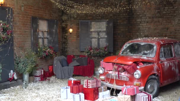 Újév és mágia Karácsonyi díszített külső retro piros autó sok ajándékot és sok ünnepi újévi fények, koszorúk házon kívül kanapéval — Stock videók