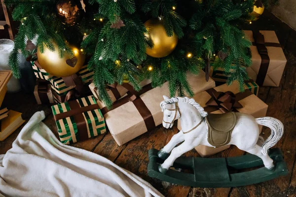 Wakacje, pudełka na prezenty noworoczne i drewniana zabawka dla koni pod ozdobioną choinką ze złotymi bombkami, girlanda w przytulnym wnętrzu poddasza. — Zdjęcie stockowe