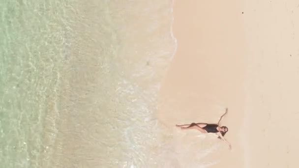 Direct boven bovenaanzicht van vrolijke glimlachende vrouw in zwarte bikini en zonnebril op het strand genietend van oceaangolven op zomervakantie. Reistropisch concept — Stockvideo