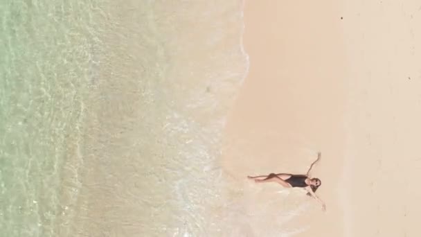 Diretamente acima da vista superior da mulher sorriso feliz em biquíni preto e óculos de sol na praia desfrutando de ondas do oceano em férias de verão. Conceito trópico de viagem — Vídeo de Stock