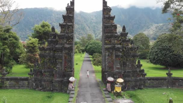 Aerial view of happy tourist woman with drone running through bali traditional gate in bedugul Traditional Balinese Hindu gate Candi Bentar close to Bedugul Bali island, Indonesia — Stock Video