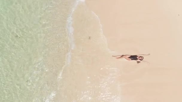 Bovenaanzicht vanuit de lucht op de vrouw in zwarte bikini liggend op het strand en bewegende handen die de golven van de oceaan aanraken tijdens de zomervakantie. inzoomen met een drone, Travel tropic concept — Stockvideo