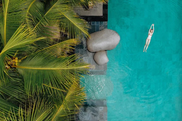 Draufsicht auf schlanke junge Frau im Bikini, die in Luxus-Pool und Palmen schwimmt. Urlaubskonzept. Drohnenfoto — Stockfoto