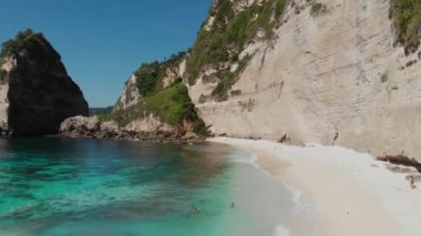 Aerial view of tropical beach, sea rocks, turquoise ocean and palm trees. Drone goes up. Atuh beach, Nusa Penida island, Bali, Indonesia. travel concept