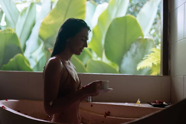 Woman sitting in stone bath tube with tropical flowers and drink herbal tea with jungle view, organic skin care, luxury spa hotel, Bali Indonesia — 스톡 사진