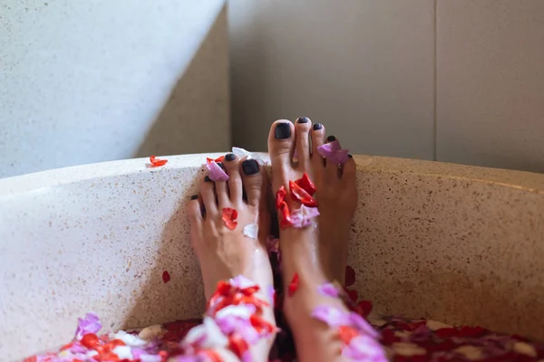 Zamknij żeńskie stopy w kąpieli na świeżym powietrzu z tropikalnych kwiatów.Spa, ekologiczne i koncepcji pielęgnacji skóry. Nogi kobiety w płatkach. — Zdjęcie stockowe