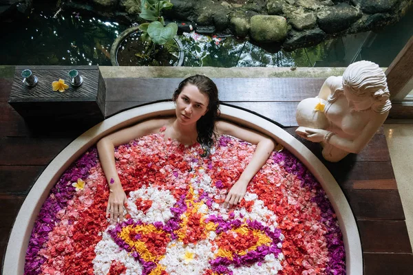 Mujer relajante en baño al aire libre redonda con flores tropicales, cuidado de la piel orgánica, hotel spa de lujo, foto estilo de vida, vista superior —  Fotos de Stock