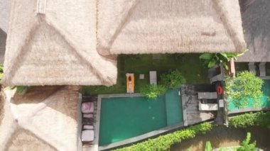 Bej bikinili, ince bir kadının havadan görünüşü rahatlıyor ve Ubud villasındaki tropik bahçede şezlongda güneşleniyor. Drone yükseliyor. Tatil kavramı.