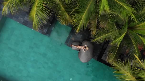 Aerial Drone Flight Widok szczupłej młodej kobiety w beżowym bikini i słomkowym kapeluszu relaksującej się w luksusowym basenie.. — Wideo stockowe