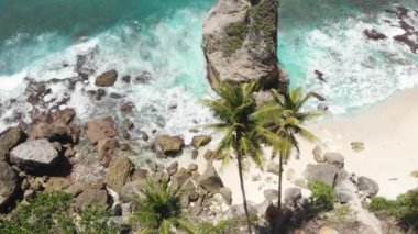 Tropik plaj, deniz taşları, turkuaz okyanus ve palmiye ağaçlarının hava aracı görüntüsü. Atuh Sahili, Nusa Penida Adası, Bali, Endonezya. Tropik arka plan ve seyahat kavramı