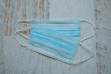 Beyaz ahşap arka planda lastik kulaklıklı iki cerrahi maske. Ağız ve burnu örtmek için tipik 3 katlı cerrahi maske. Bakterilerin prosedür maskesi. Koruma kavramı