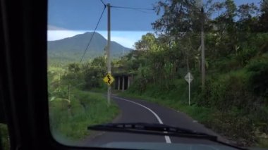 Güneşli bir günde Endonezya 'nın Bali adalarında arabasının önünden geçen virajlı bir yolun videosu..