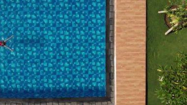 Kırmızı mayo giymiş, açık mavi suyu tropik bir havuzda yüzen bir kadının tam üstünde. Tatil konsepti. Havadan üst görünüm.