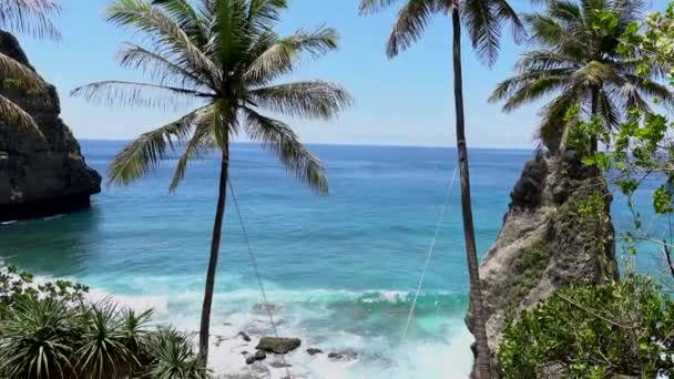 Flygdrönare utsikt över tropiska stranden, hav stenar, turkos hav och kvinna svänger mellan palmer. Stranden Atuh, ön Nusa Penida, Bali, Indonesien. — Stockvideo