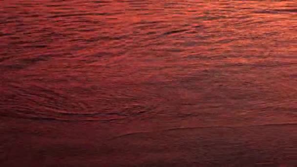 Primer plano de vídeo de olas suaves rodando en la puesta del sol luz de color naranja en la playa de arena volcánica negro océano, Bali, Indonesia — Vídeos de Stock