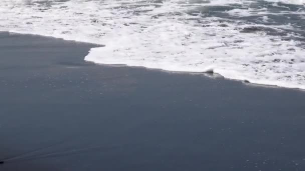 Primer plano de vídeo de olas con espuma rodando hasta la playa de arena volcánica negro océano, Bali, Indonesia — Vídeo de stock