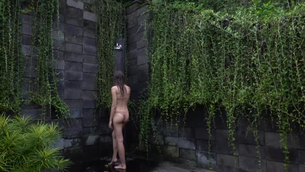 Brunetka w beżowym bikini, biorąca prysznic w tropikalnym, zielonym ogrodzie Bali. Świeże plamy czystej wody. Luksusowe spa w kurorcie. Relaks pod prysznicem na świeżym powietrzu na wakacjach — Wideo stockowe