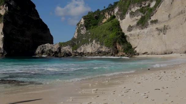 Vista da praia tropical selvagem com areia branca e ondas com espuma de mar turquesa e rochas marinhas e penhasco no fundo. Atuh beach, Nusa Penida island, Bali, Indonesia. Conceito de viagem . — Vídeo de Stock