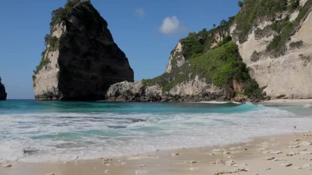 Kadının arka görüntüsü okyanus kıyısında kayalar ve turkuaz okyanusla mavi gökyüzüyle mutlu bir şekilde koşuyor. Atuh Sahili, Nusa Penida Adası, Bali, Endonezya. Tropik seyahat kavramı. — Stok video