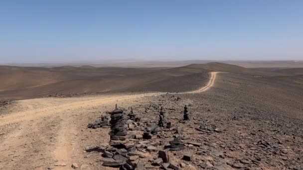 モロッコの無人風景に沿って道路に沿って禅スタイルで垂直方向に一緒に小さな石のピラミッドを配置しました。バランスと調和の概念. — ストック動画