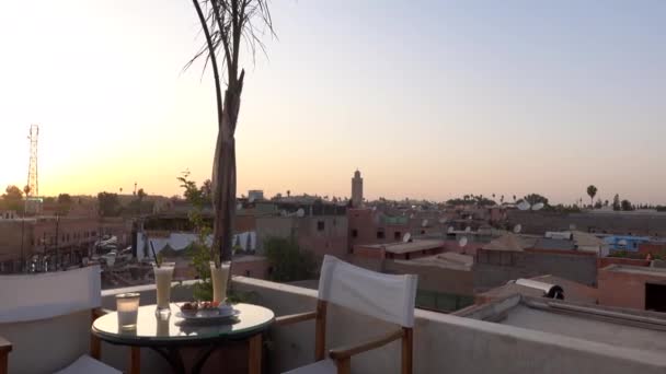 Café en la azotea con mesa en la terraza con dos cócteles al atardecer con vistas a la ciudad vieja de Marrakech, Marruecos — Vídeos de Stock