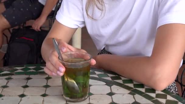 Nierozpoznawalna Europejka pije tradycyjną marokańską herbatę miętową i siedzi przy stole z dachówkami, Maroko. — Wideo stockowe