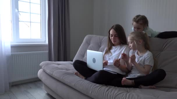 家庭では週末にソファに座ってモバイルデバイスを一緒に使用しています。母親と2人の子供の娘がスマートフォンを持ち — ストック動画