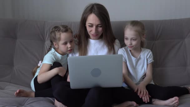 家庭では週末にソファに座ってモバイルデバイスを一緒に使用しています。母親と2人の子供の娘がスマートフォンを持ち — ストック動画