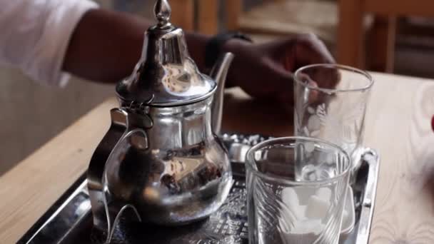 Muž ruční nalévání čaje z zdobené stříbrné konvice do sklenic na malém stolku podle marocké tradice. Rituální příprava mátového čaje v Maroku — Stock video