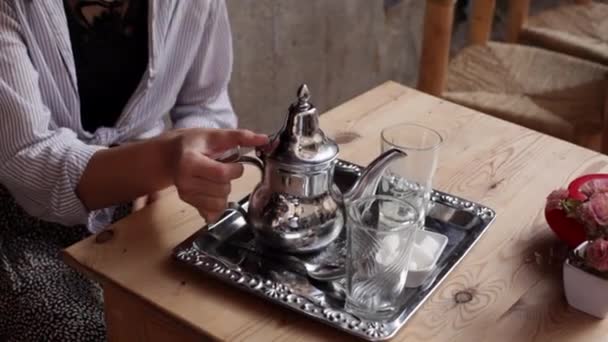 Mulher mão derramando chá de hortelã de bule de prata ornamentado em copos em pequena mesa de acordo com a tradição marroquina. Preparação ritual de chá em Marrocos — Vídeo de Stock