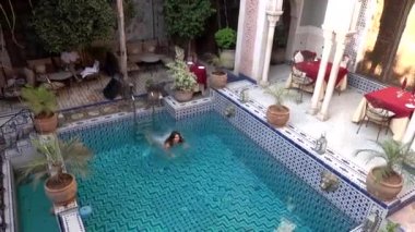 Fas 'ın lüks avlusunda havuzda yüzen bir kadın. Geleneksel Arap mimarisi ile dolu. Mozaik iç mimari..
